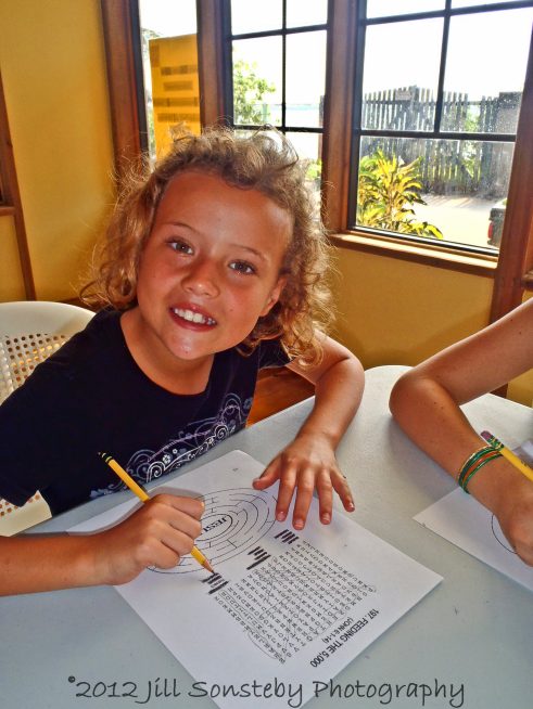 A little girl is smiling as she works on a word search and maze.